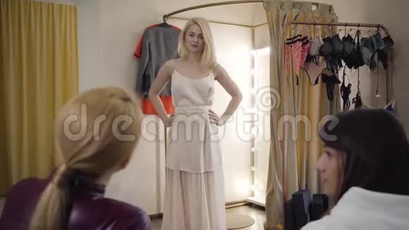 年轻的金发白种人的肖像穿着新的米色连衣裙向朋友展示服装支持女孩的后景视频的预览图