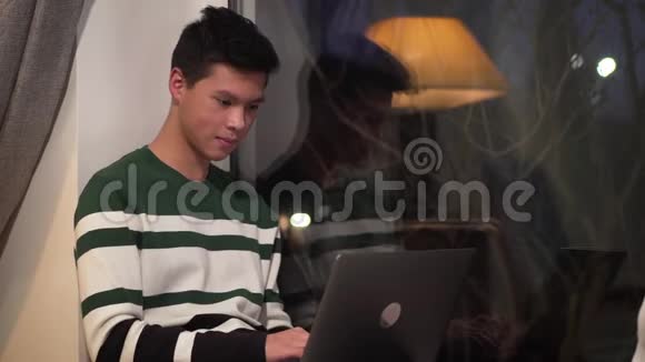 快乐的亚洲男性青少年坐在窗台上使用笔记本电脑漂亮的大学生在键盘和键盘上打字视频的预览图