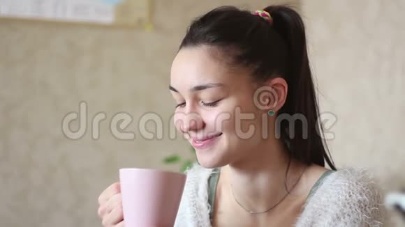 一个年轻迷人的女孩正从粉红色的杯子里喝咖啡微笑着看着相机视频的预览图