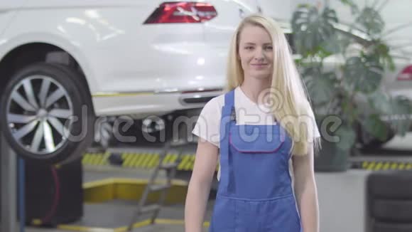 中镜头的年轻白种人女人交叉双手和微笑金发女汽车修理工在工作场所摆姿势视频的预览图