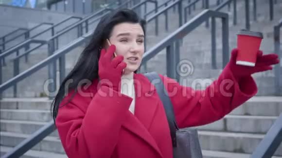 镜头跟踪年轻白人妇女在户外打电话穿红色外套和手套的时髦女孩等待视频的预览图