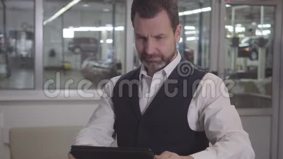 年轻的高加索男性维修店经理坐在汽车背景下的平板电脑的肖像成功的男人视频的预览图