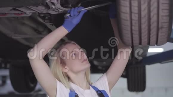 年轻白种人女人站在车下和拧紧车轮螺丝的肖像女汽车修理工视频的预览图