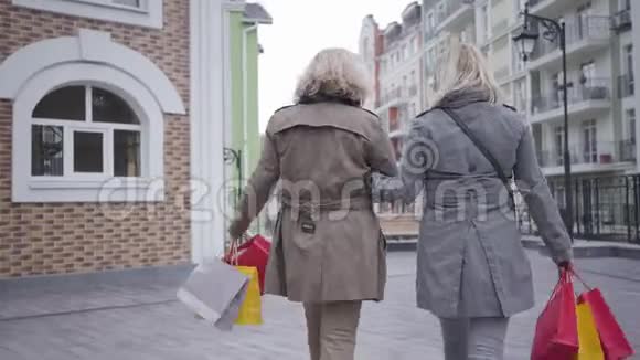 两名白人女性带着购物袋坐在长椅上沿着城市街道行走拍摄快乐镜头视频的预览图