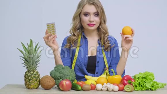 一张桌子上的女人拿着橘子和药丸放在水果和蔬菜的背景上视频的预览图