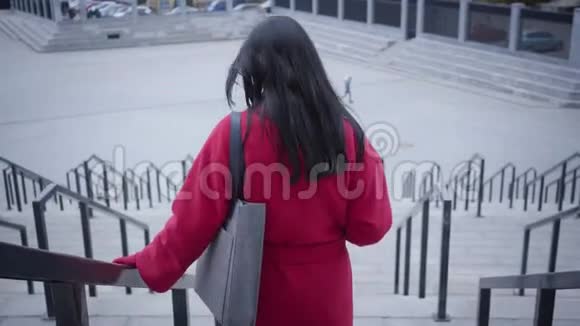 后景优雅的年轻女士穿着红色外套走下楼梯自信的白人女人黑发漫步视频的预览图