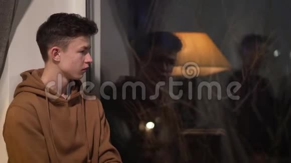 侧观年轻的黑发白种人男孩坐着看着窗外令人不安的男孩独自度过一个晚上悲伤视频的预览图