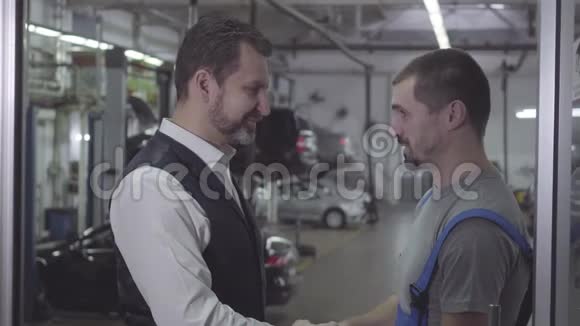 侧视特写两名白人男子握手在修理店和交谈汽车修理工和客户视频的预览图
