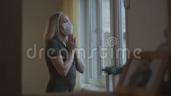 戴着医用面具的女人用双手在窗前祈祷视频的预览图