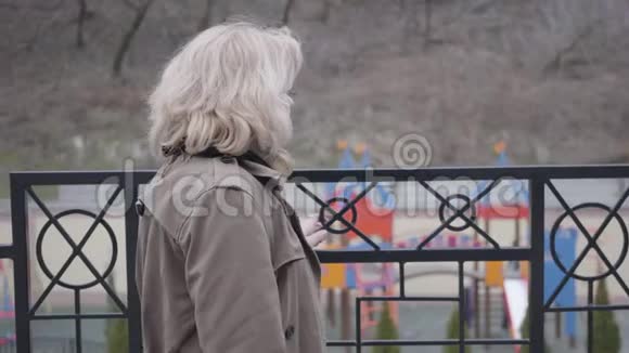 站在栅栏旁边看着远处沉思的高加索族妇女金发成熟女性退休人员视频的预览图
