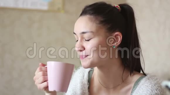 一个年轻迷人的女孩正从粉红色的杯子里喝咖啡微笑着看着相机视频的预览图