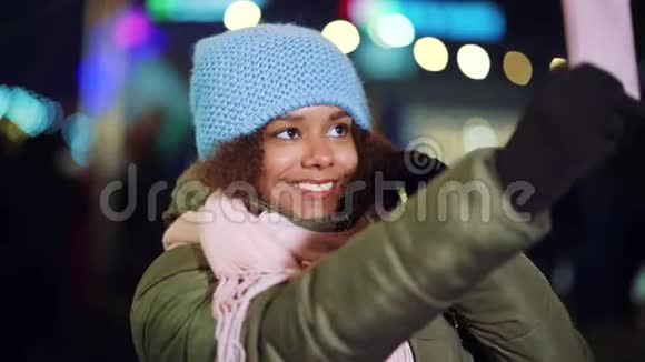 迷人的黑人女孩晚上在圣诞市场录制自拍视频视频的预览图