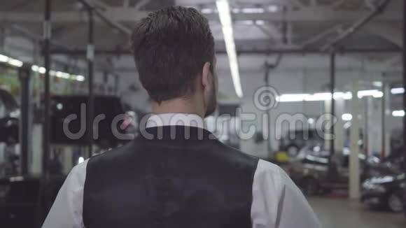 后景白人男子穿着背心和衬衫站在修理店和看汽车自信的年轻商人视频的预览图