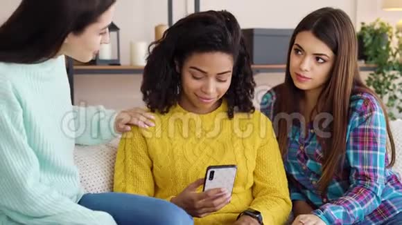 多种族女孩支持朋友坐在家里用智能手机视频的预览图