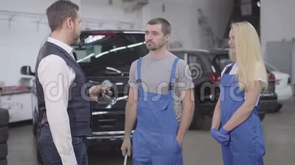 成年白种人商人在修理店给汽车机械师送车钥匙男女专业人员视频的预览图