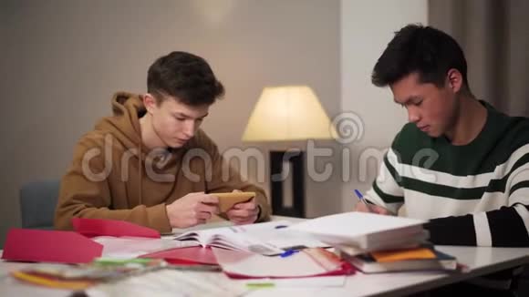 十几岁的白人男孩分散了他的亚洲同伴的注意力两个男大学生坐在桌边视频的预览图