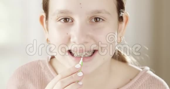 漂亮的小女孩用牙间刷清洁牙套同时看着镜子微笑牙齿矫正器视频的预览图