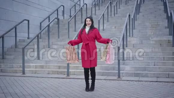 在城市楼梯的背景下兴奋的高加索女人带着购物袋跳舞的长镜头时尚年轻视频的预览图