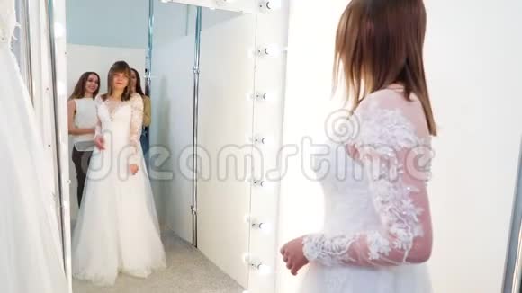 在沙龙里新娘穿着婚纱和可亲的朋友一起照镜子视频的预览图