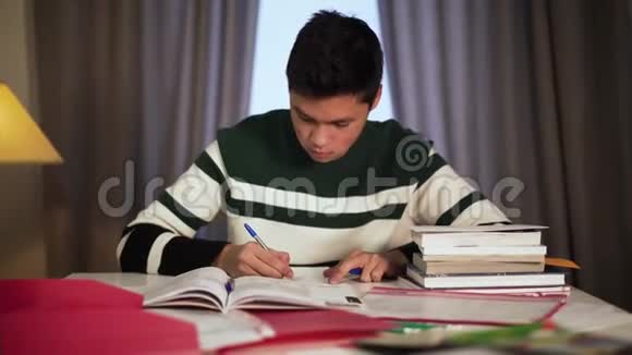 集中亚洲男孩在餐桌上学习的肖像漂亮的年轻大学生在室内写作业簿视频的预览图