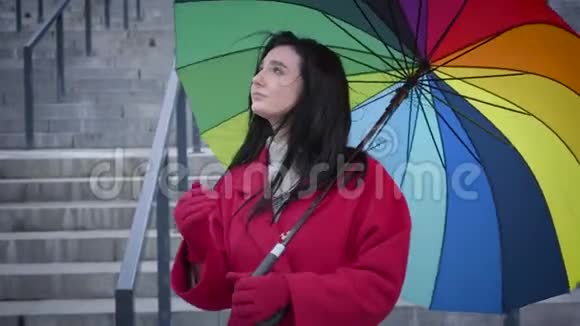 相当开朗的白人女人折叠伞和看相机穿着红色外套享受小雨的快乐女士视频的预览图