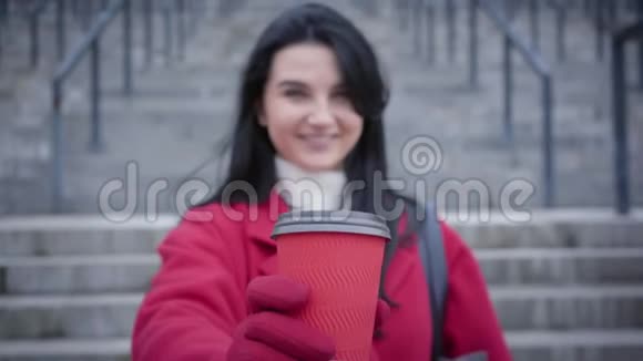 无法辨认模糊的白种人女人把咖啡杯伸到镜头前微笑穿红色外套和手套的年轻女士视频的预览图