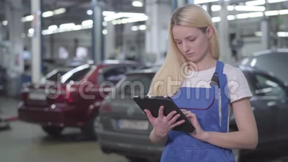 年轻的白种人妇女穿着工作长袍拿着平板电脑微笑着的肖像漂亮的专业汽车技工视频的预览图