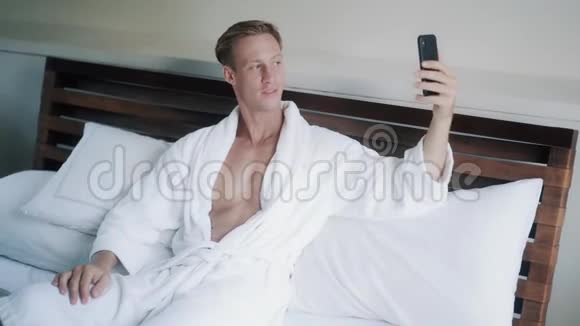 金发帅哥在床上用手机打可视电话视频的预览图