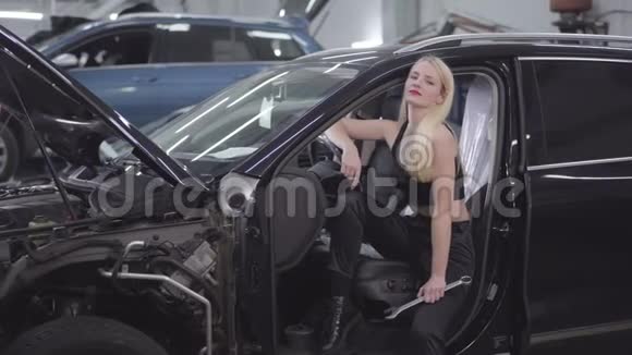 漂亮的白种人金发女人在驾驶座上摆着可调节的扳手漂亮的汽车修理工视频的预览图