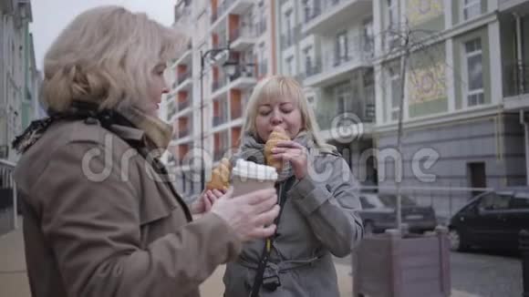 高加索族妇女在城市街头喝咖啡吃牛角面包退休人士在户外休息视频的预览图