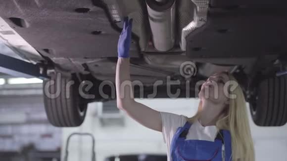 有信心的白种人汽车机械师检查固定汽车的底部视图在汽车修理店工作的金发女郎视频的预览图