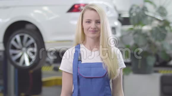 年轻白种人妇女站在修理厂白车背景下的肖像女汽修工视频的预览图