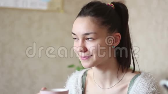 一个年轻迷人的女孩在家里坐在床上时喝着粉红色杯子里的咖啡视频的预览图