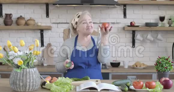 快乐的高加索族女人在厨房里手里拿着黄瓜和番茄旋转的肖像积极成熟视频的预览图
