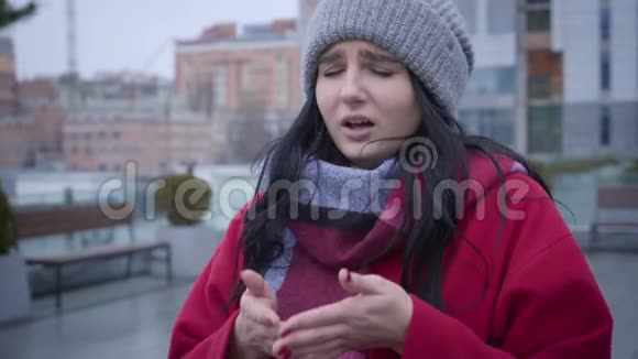 穿着红色外套和温暖帽子在户外打喷嚏的病态白人女孩的特写照片年轻漂亮的女人得了流感视频的预览图