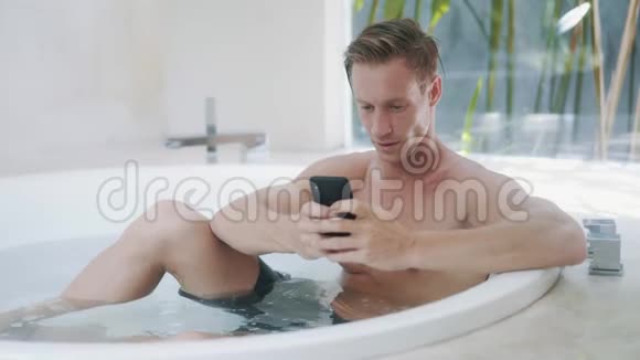 年轻人在现代浴缸里用智能手机阅读信息视频的预览图