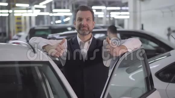 镜头慢慢地围绕着成年白种人商人站在旁边竖起大拇指打开车门成功的男人视频的预览图
