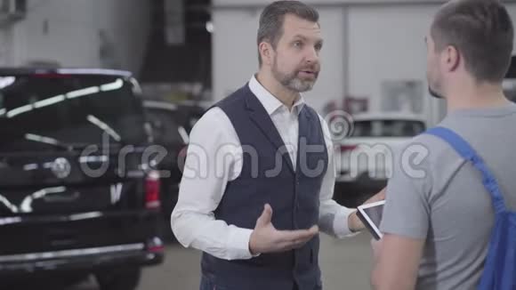 镜头接近面对愤怒的白种人客户在修理店与汽车机械师交谈帅哥大人视频的预览图