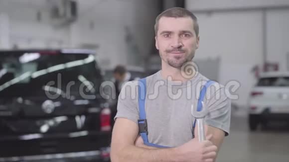 年轻英俊的白种人看着镜头微笑的肖像专业的汽车技师在工作场所摆姿势视频的预览图