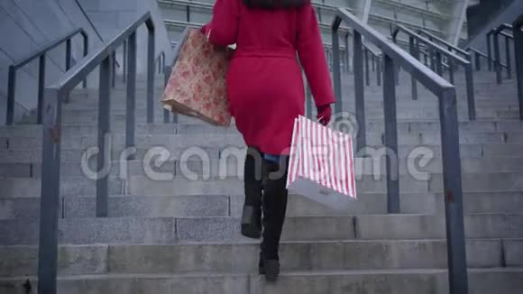 镜头跟随不可辨认的时尚女士穿着红色外套和黑色靴子在城市的楼梯上购物视频的预览图