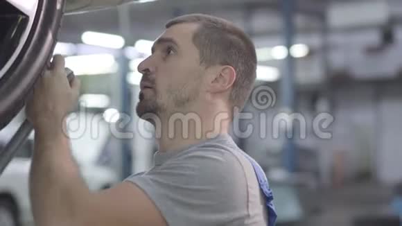 汽车车轮上男性白种人汽车机械拧紧螺钉的特写在修理店工作的年轻人专业人员视频的预览图
