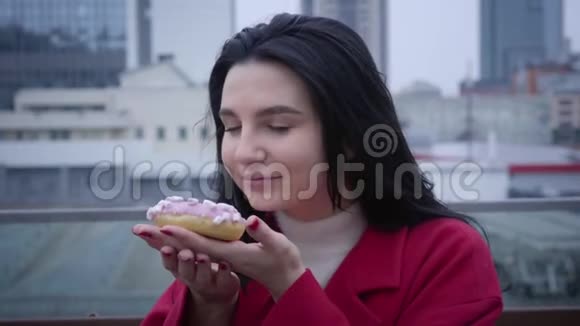 特写照片年轻微笑的高加索女人闻着甜甜圈看着镜头性格开朗的女人视频的预览图
