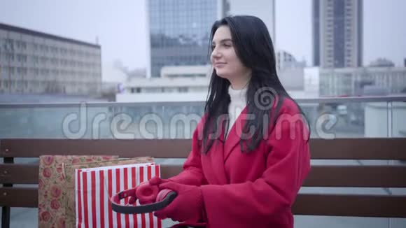 在城市里一个开朗的白种人女人戴上耳机听音乐穿红色外套的积极女孩视频的预览图