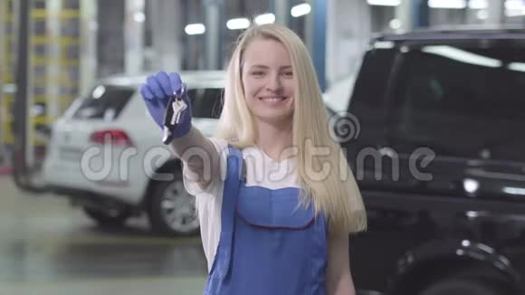 带着微笑的金发白种人女人的肖像她展示了汽车钥匙的镜头年轻的女汽车修理工对她的工作很满意视频的预览图