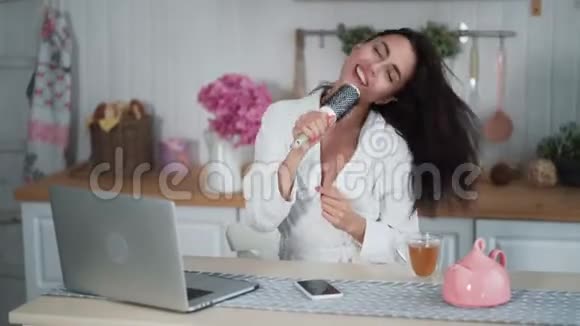 穿着浴袍的年轻女子在厨房里用梳子唱歌视频的预览图