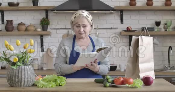 积极的白人高级妇女寻找新的沙拉配方站在厨房美丽中年画像视频的预览图