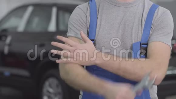 不可辨认的白种人穿着蓝色工作袍在黑色汽车的背景下用扳手交叉双手男性视频的预览图