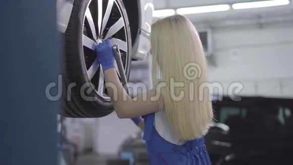 侧面观看金发白种人妇女拧紧车轮螺丝在修理厂工作的年轻女汽车修理工视频的预览图