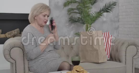 成熟的白人金发女人拿起电话看着购物袋快乐的高级女购物者聊天视频的预览图