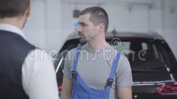 年轻白种人汽车修理工在修理店与顾客交谈的肖像棕色眼睛的帅哥在讨论视频的预览图